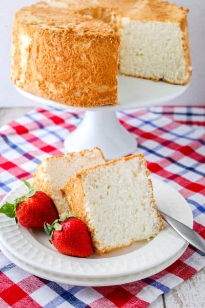 slices of angel food cake on a plate with strawberries and a fork with the rest of the cake behind them