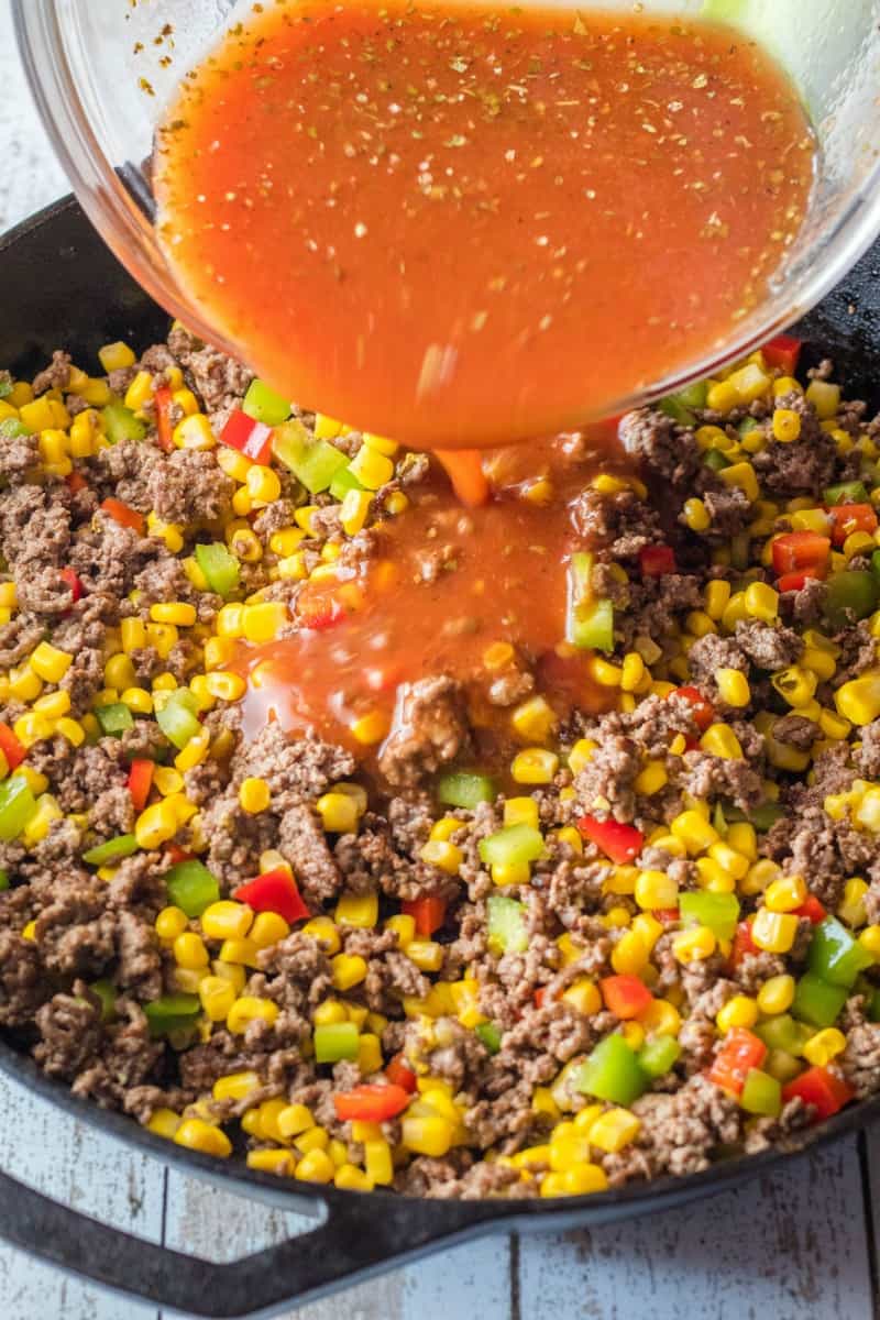 sloppy joe sauce being poured over ground beef and veggies