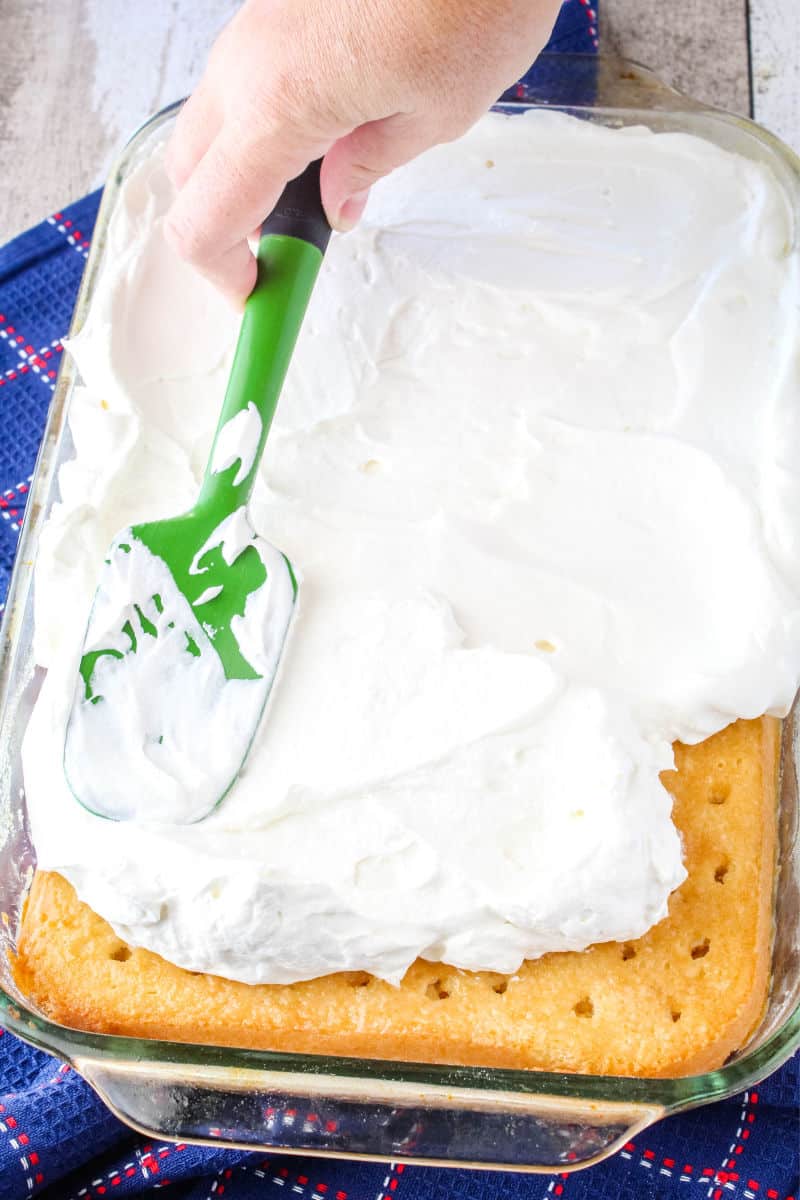 whipped cream being spread over a poke cake