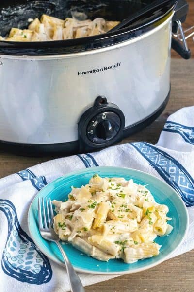 Crock Pot Chicken Alfredo served on a plate with crock pot behind it