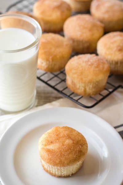 cinnamon sugar muffin on a plate next to a glass of milk with more muffins in background