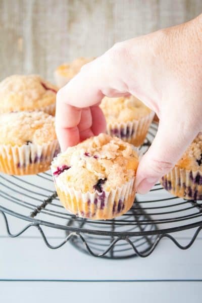hand picking up a blueberry muffin from a cake stand