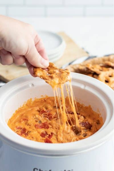 pretzel chip with crock pot pizza dip being pulled out of a slow cooker with cheese strings hanging down