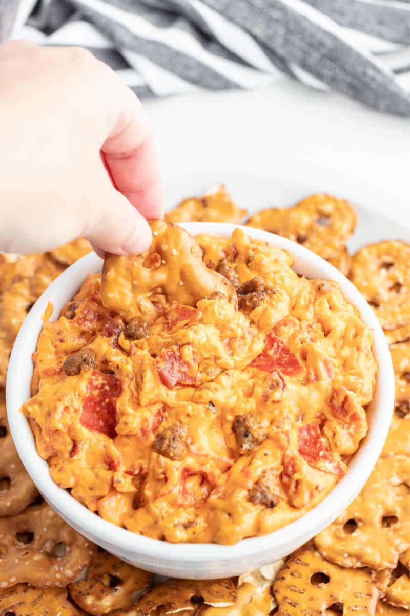 pretzel chip being dipped into a bowl of meat lover's crock pot pizza dip