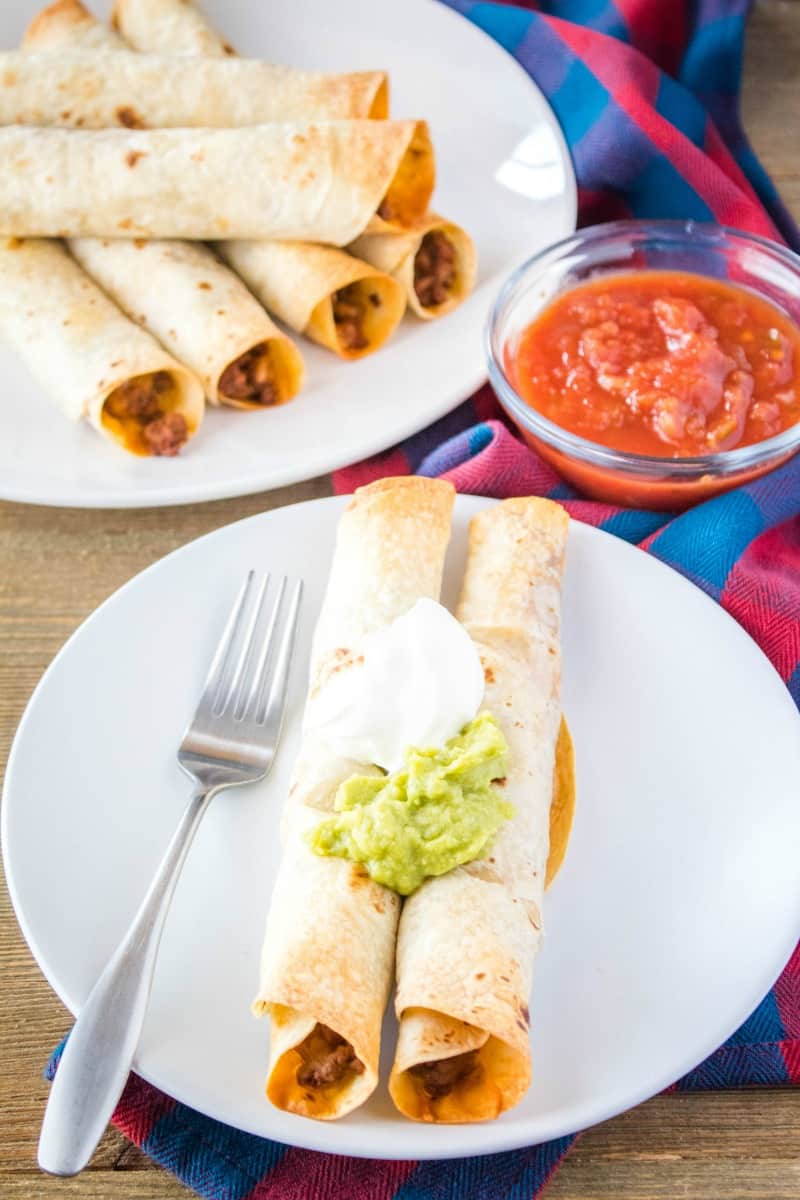 easy baked beef taquitos on a plate topped with sour cream and guacamole