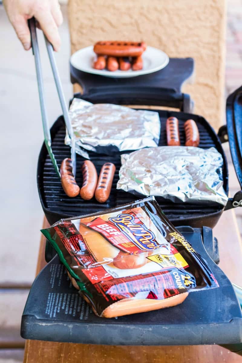 man grilling hot dogs and foil packs on tabletop grill