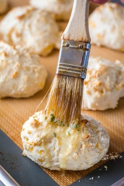 garlic butter being brushed on cheddar biscuits