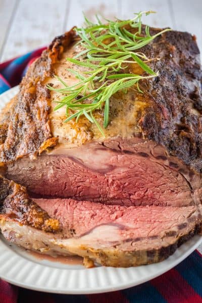 sliced prime rib on a serving platter with rosemary