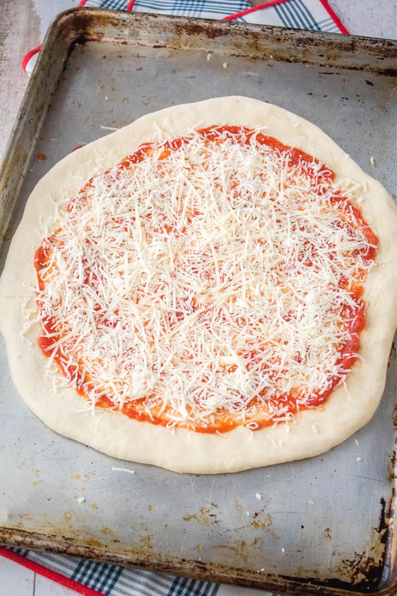 pizza sauce and mozzarella cheese on pizza dough on a baking sheet