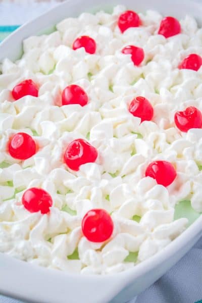 lime jello salad topped with whipped cream and cherries