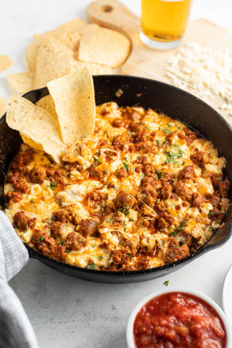two tortilla chips stuck into a skillet of queso fundido con chorizo with a small bowl of salsa on the side