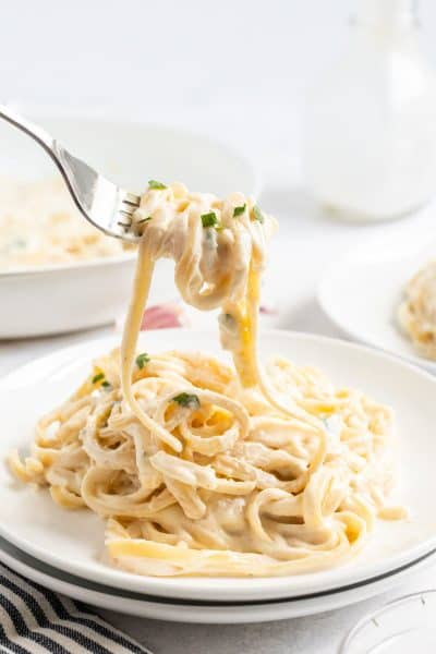 forkful of fettuccine alfredo over a plate of pasta