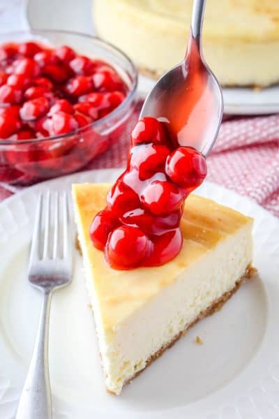 cherry pie filling being spooned over a slice of new york cheesecake