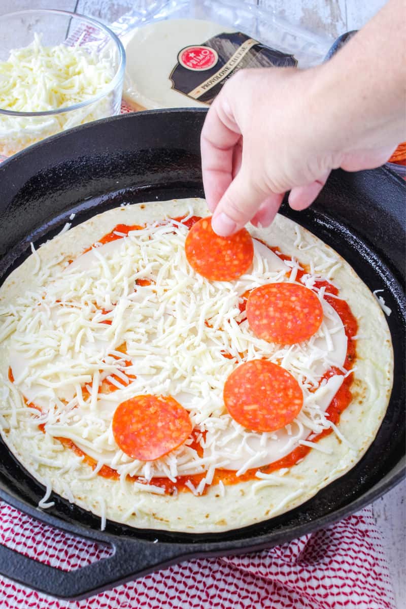 pepperonis being placed on top of cheese for a skillet tortilla pizza
