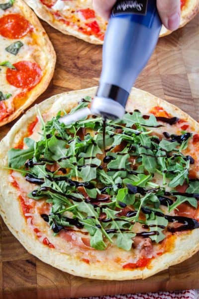balsamic gaze being drizzled over a tortilla pizza with prosciutto and arugula