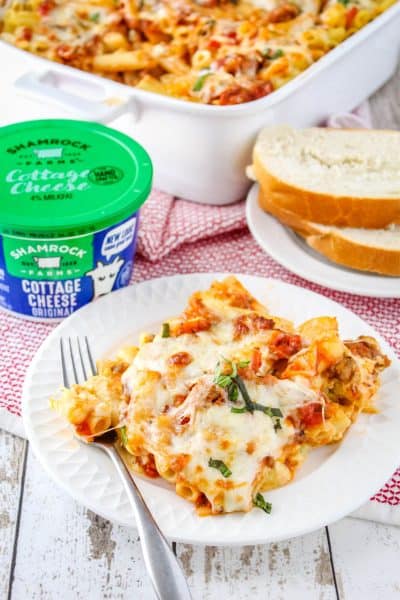 portion of baked ziti on a plate with some sliced bread and a tub of Shamrock Farms cottage cheese