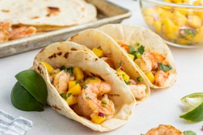 grilled shrimp tacos with mango salsa being held up by lime wedges