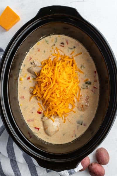 cooked crock pot chicken in sauce with shredded cheese on top