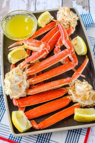 snow crab leg clusters on a plate with clarified butter and lemon wedges