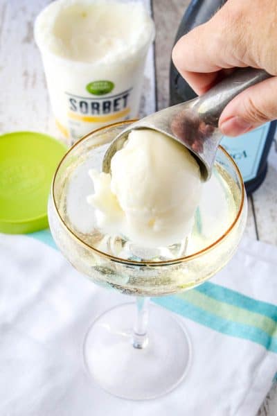 scoop of lemon sorbet in an ice cream scoop being put into a cocktail glass