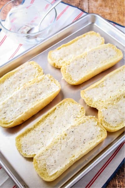hoagie rolls on a baking sheet with garlic butter spread over cut sides