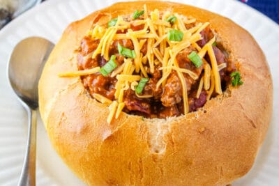 bread bowl with chili on a plate with a spoon