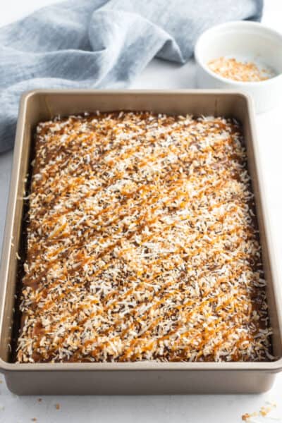 samoa poke cake topped with toasted coconut and drizzled with caramel sauce