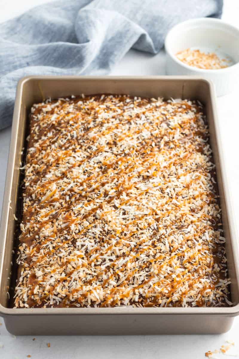 samoa poke cake topped with toasted coconut and drizzled with caramel sauce
