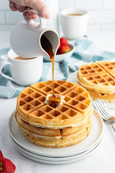 syrup being poured over a stack of waffles