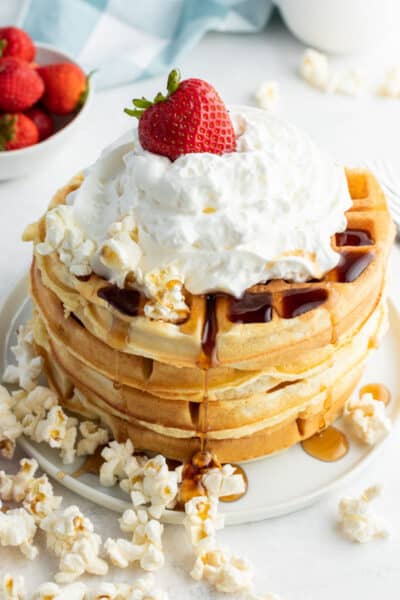 stack of waffles with syrup, popcorn, whipped cream, and a strawberry on top to make together breakfast