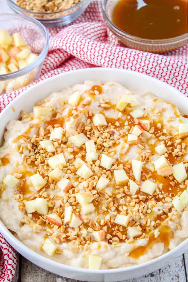 cheesecake dip topped with caramel sauce, chopped nuts, and diced apples