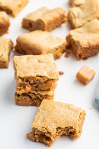 caramel pecan blondies on a counter with a couple stacked up and one with a bite taken out