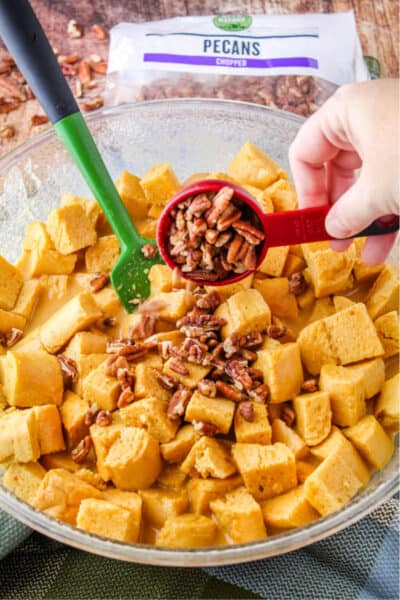chopped pecans being added to bread cubes coated in pumpkin custard