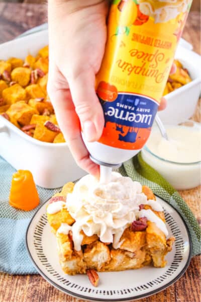 Lucerne pumpkin spice whipped cream being squirted onto a piece of bread pudding