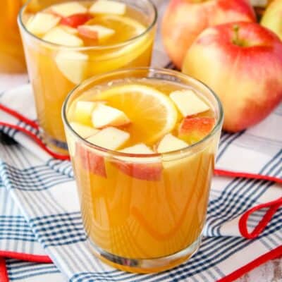 square image of apple cider whiskey punch in a rocks glass with apples and an orange slice