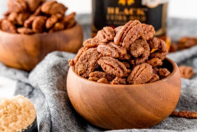 candied pecans in a wooden bowl on a grey cloth napkin next to a cup of brown sugar