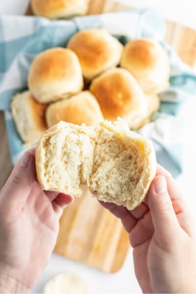 hands pulling open a dinner roll to show texture inside