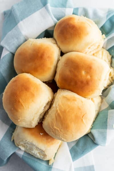looking down at a basket of dinner rolls with a blue plaid cloth napkin underneath them