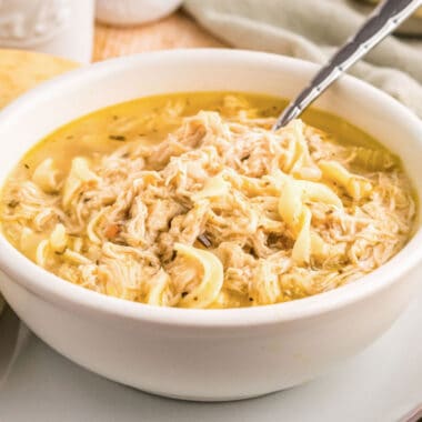 square image of crock pot chicken noodle soup in a bowl with a spoon