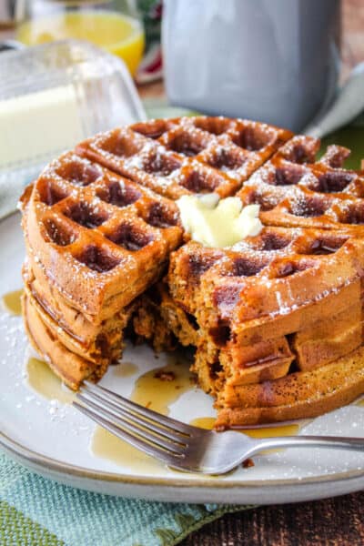 stack of gingerbread waffles on a plate with a fork and a portion cut out