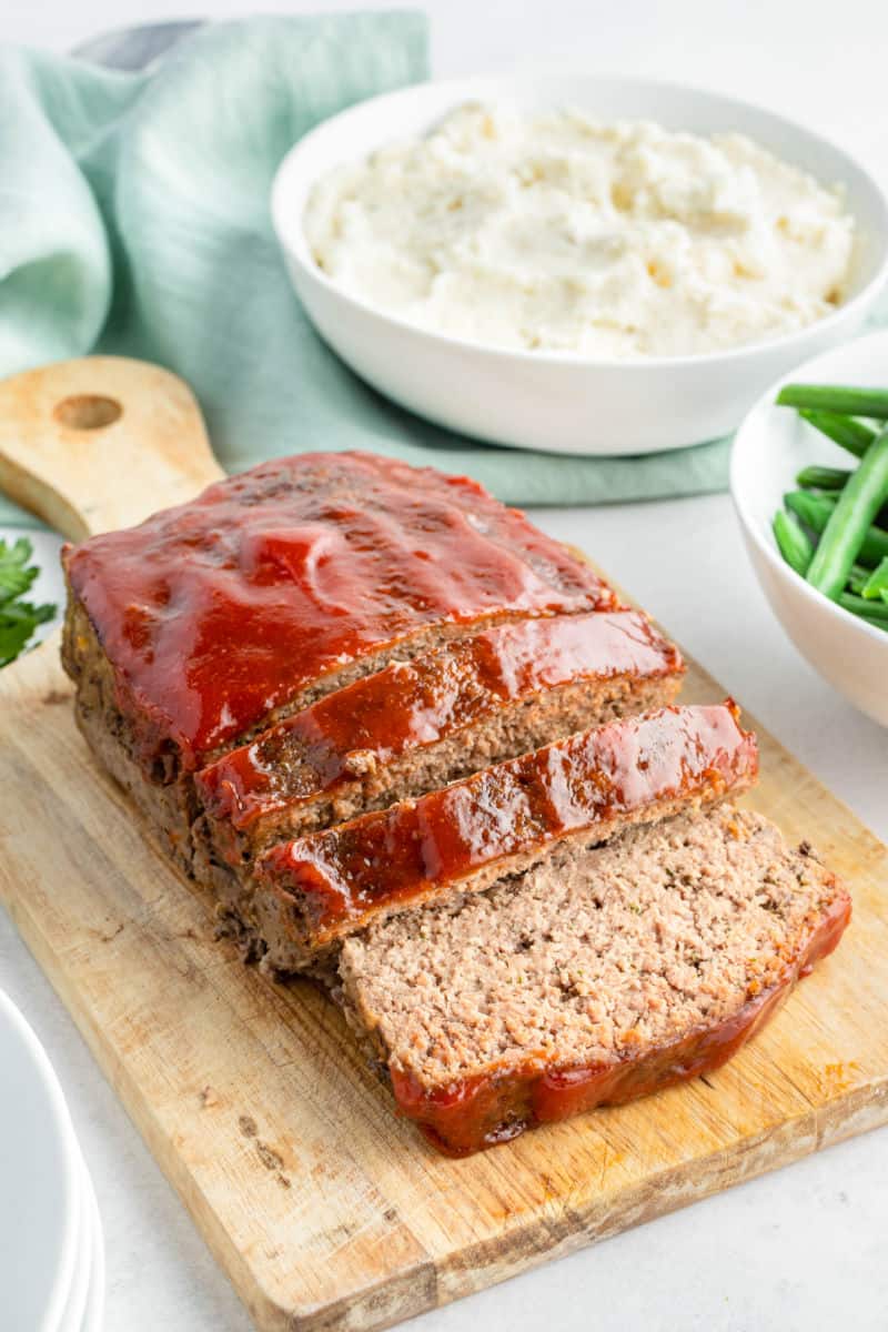 cooked meatloaf with glaze on a cutting board with a few slices cut