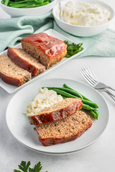 two slices of meatloaf on a plate with mashed potatoes and green beans