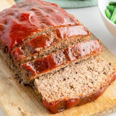 square image of meatloaf on a cutting board with a few slices cut