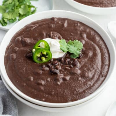 square image of black bean soup in a bowl with jalapeno slices, sour cream, and cilantro
