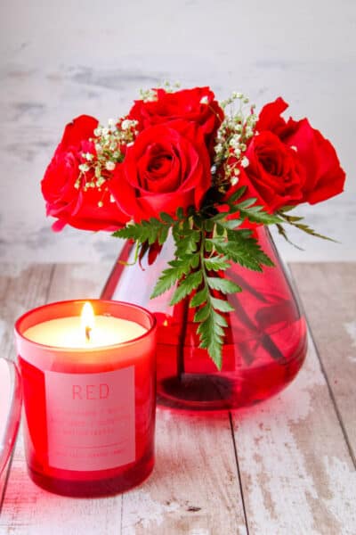 small bouquet of red roses in a red teardrop vase next to a red candle