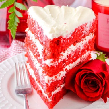 square image of a red velvet cake splice on a plate with a fork and rose