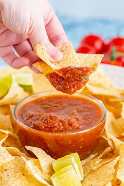 hand holding chips above a bowl of homemade salsa after dipping