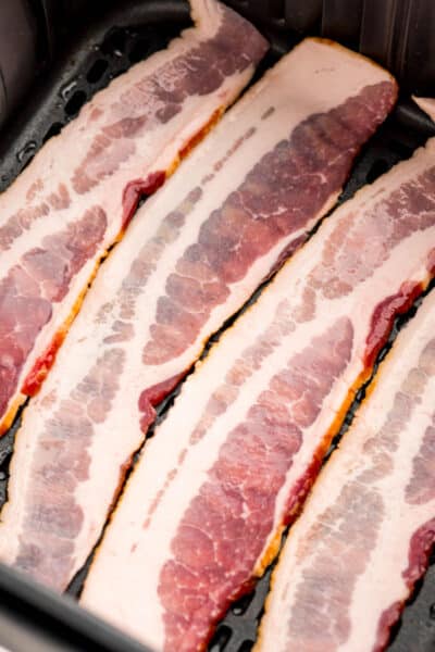 close up of raw strips of bacon in an air fryer basket
