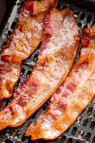 close up of strips of bacon in an air fryer basket halfway through cooking