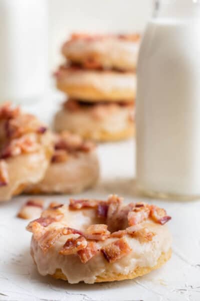 ample bacon donut in front a of a stack of donuts and a glass bottle of milk